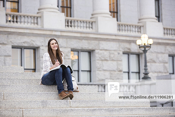 Smiling Caucasian woman sitting on staircase holding notebook