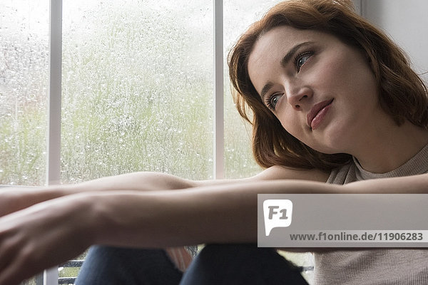 Kaukasische Frau sitzt in der Nähe von regnerischen Fenster Tagträumen
