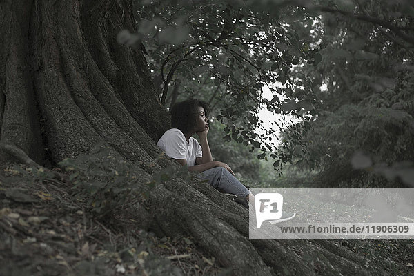 Nachdenkliche Frau sitzt auf Baumwurzeln im Wald