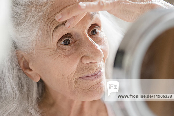 Ältere Frau überprüft Augenfalten im Spiegel