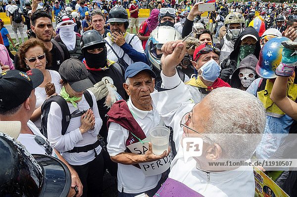 A priest blesses demonstrators on the freeway. Opposition protesters assembled on the Francisco Fajardo motorway  near Francisco de Miranda Air Force Base in La Carlota  to demand that the Bolivarian National Armed Forces (FANB) - peacefully - end the brutal repression  after being assassinated David Vallenilla last Thursday by an Aviation official. Caracas  June  24  2017.