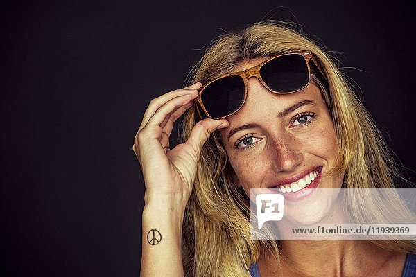 Young woman lifting sunglasses and smiling cheerfully at camera  portrait
