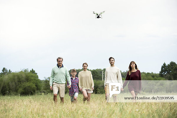 Familie geht zusammen im Feld  während die Drohne über Kopf fliegt.