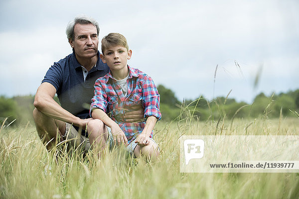 Father and son crouching together in tall grass