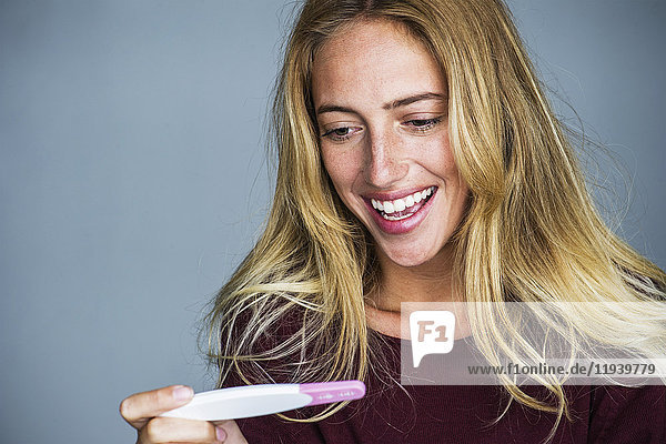 Junge Frau schaut auf Schwangerschaftstest und lächelt