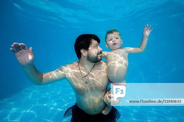 Dad and son playing under water in the pool.