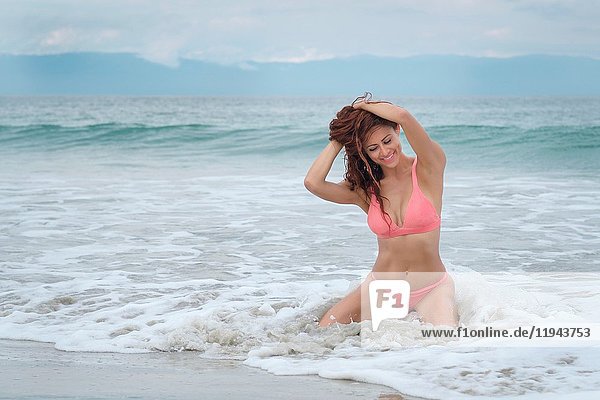 Hispanic woman in bikini smiling happily while sitting in the water.