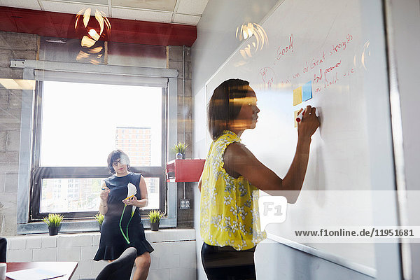 Zwei Frauen im Büro  Problem lösen  Whiteboard benutzen  Haftnotizen auf Whiteboard kleben