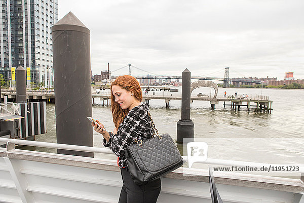Junge Geschäftsfrau auf dem Fährdeck mit Blick auf Smartphone  New York  USA