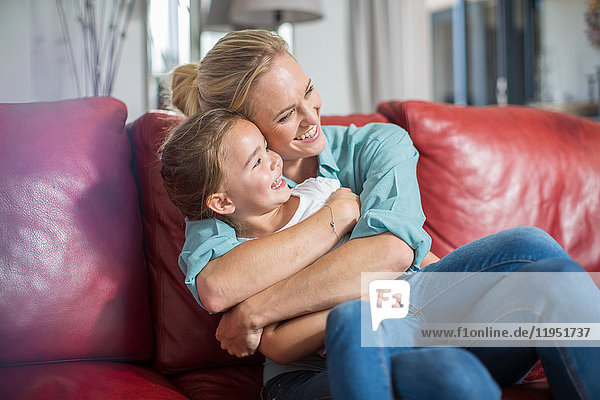 Mother and daughter on sofa cuddling and smiling