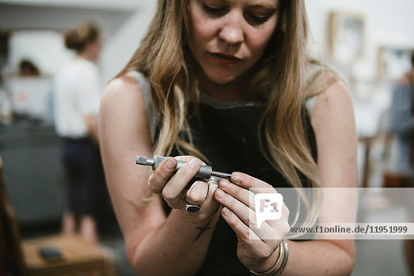 Female jeweller using hand tool in jewellery workshop