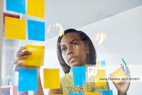 Young woman in office  sticking sticky notes to glass in office