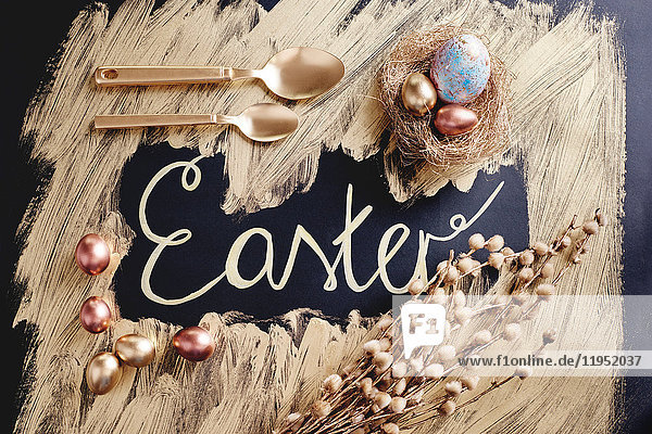Draufsicht auf gefärbte und goldbemalte Ostereier und -löffel mit handgeschriebenen Ostern
