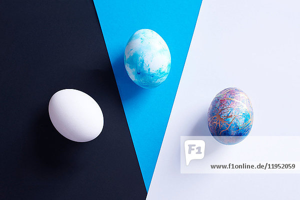 Overhead view of three dyed easter eggs on blue  black and white shapes