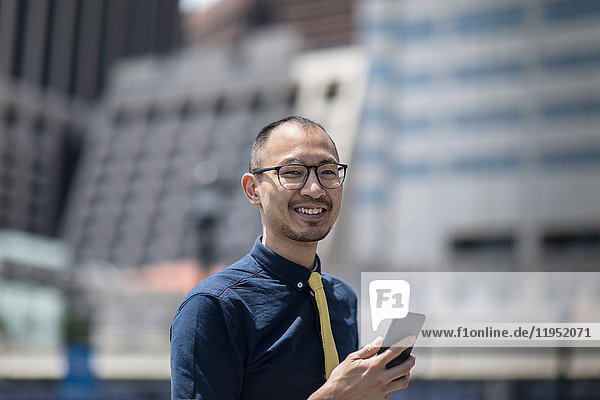 Portrait of smiling businessman with smartphone outside office building  New York  USA