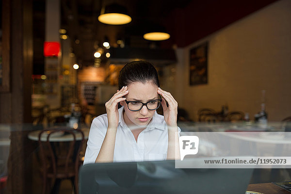 Woman in coffee shop using laptop looking stressed