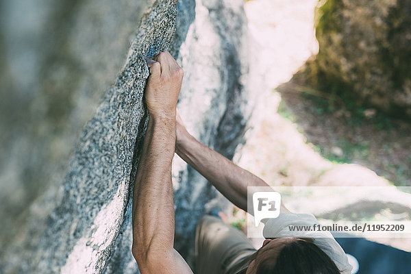 Hochwinkelaufnahme eines jungen männlichen Boulderers  der einen Felsbrocken greift  Lombardei  Italien