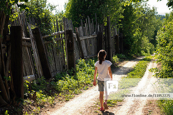 Rückansicht eines einsamen Teenager-Mädchens  das auf einem ländlichen Feldweg spazieren geht