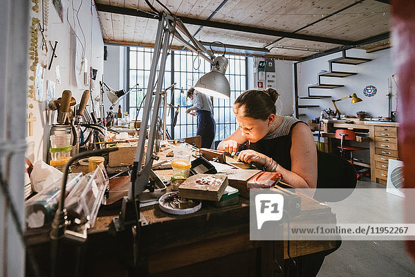 Female jeweller engraving metal at workbench