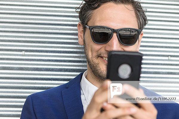Junger Geschäftsmann mit Sonnenbrille schaut auf Smartphone