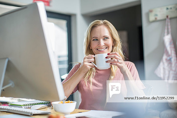 Frau am Computer beim Kaffeetrinken lächelnd