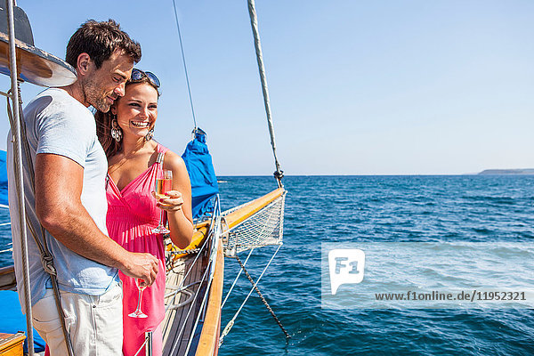 Paar steht auf dem Boot  auf dem Wasser  hält Sektflöten in der Hand  schaut auf die Aussicht