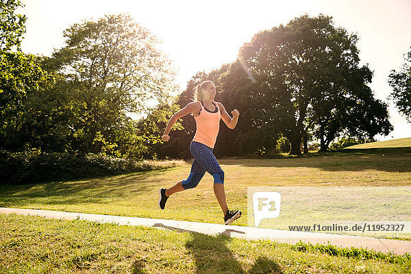 Junge weibliche Läuferin läuft im Sonnenlicht den Parkweg entlang