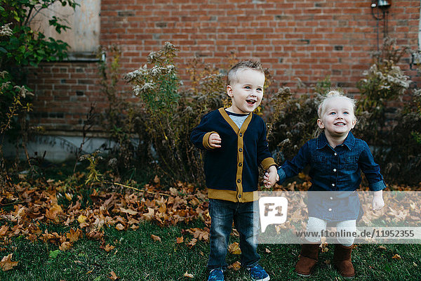 Happy male and female toddler twins holding hands in garden