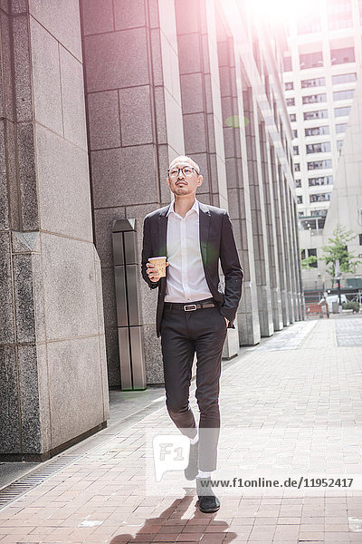 Cool businessman with takeaway coffee strolling along sidewalk  New York  USA
