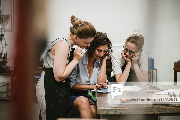 Three female jewellers looking at digital tablet at workbench meeting