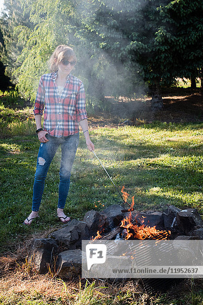 Frau steht am Lagerfeuer   kocht Würstchen in Flammen