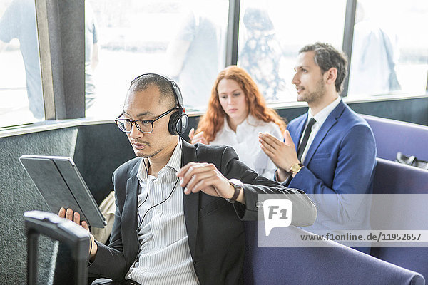 Geschäftsmann  der auf der Passagierfähre Kopfhörer hört und auf ein digitales Tablet schaut