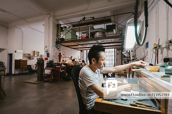 Männlicher Juwelier  der an der Werkbank einer Schmuckwerkstatt arbeitet