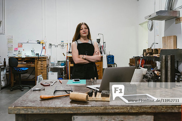 Portrait of female jeweller with arms folded in jewellery workshop