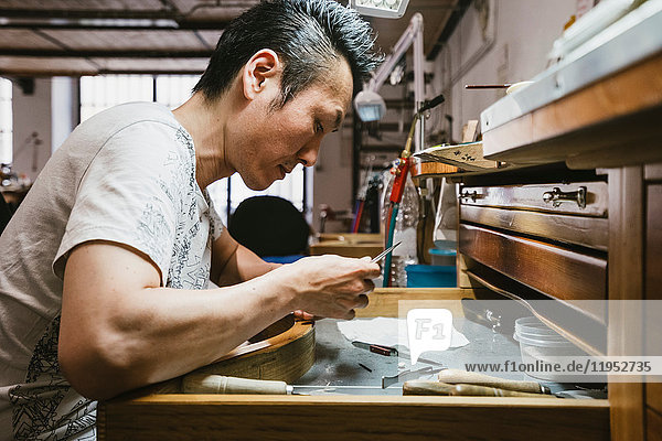 Male jeweller inspecting metal at workbench