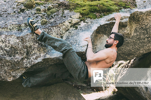 Bare chested male boulderer climbing boulder overhang  Lombardy  Italy