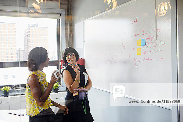 Two women in office  solving problem  using whiteboard  sticky notes stuck on whiteboard
