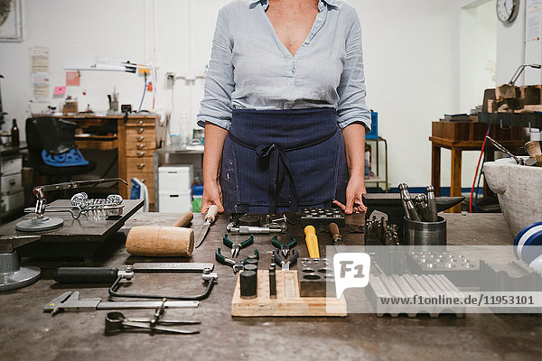 Mid section of female jeweller laying out hand tools at workbench in jewellery workshop