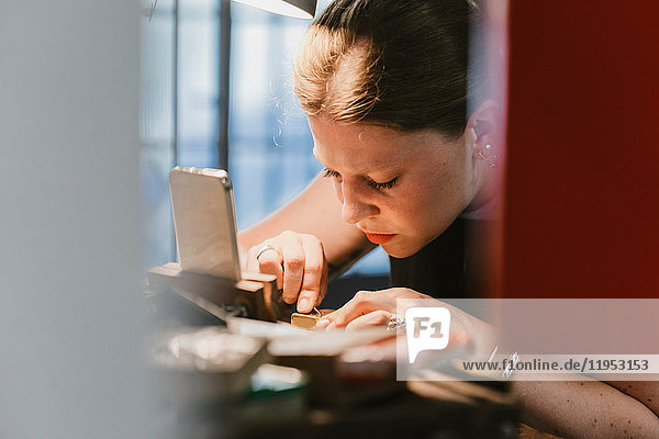 Female jeweller engraving metal at workbench