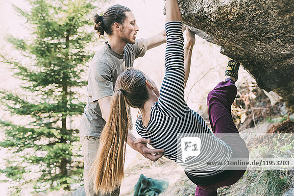 Young male boulderer supporting woman climbing boulder  Lombardy  Italy