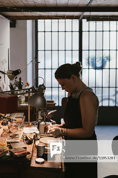 Female jeweller polishing jewellery at workbench