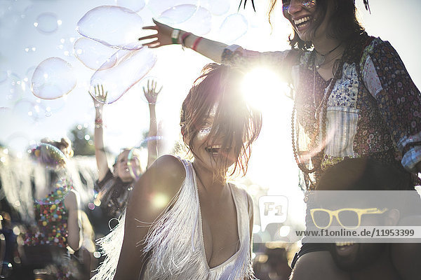 Schwelgender junger Mann mit gelber Sonnenbrille und Frau auf den Schultern bei einem Sommer-Musikfestival.