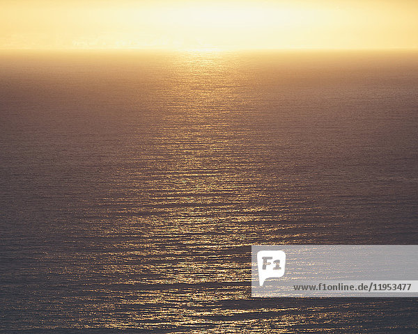 Blick vom Land über den Ozean bis zum Horizont. Die Sonne ruht am Horizont und das vom Wasser reflektierte Licht.