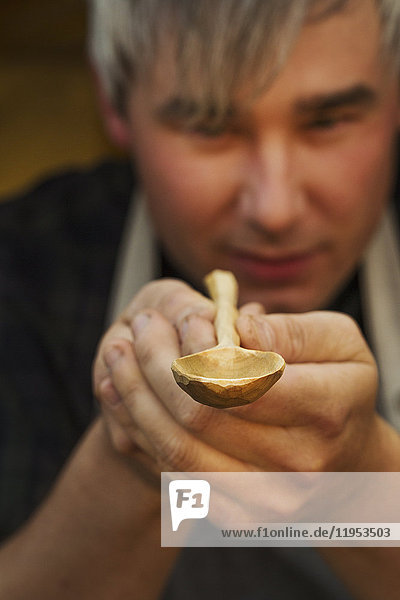 Ein Handwerker  der einen handgefertigten  handgemachten Holzlöffel mit langem  schlanken Stiel und runder  polierter Schale hält und inspiziert.