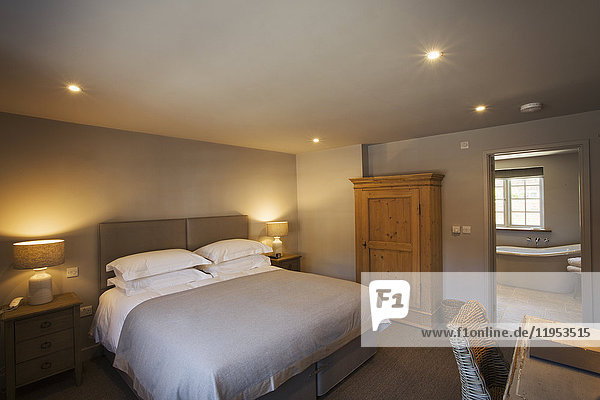 Ein gemütliches  in neutralen Farben dekoriertes Schlafzimmer mit einem Doppelbett und eingeschalteter Nachttischbeleuchtung. Gastfreundschaft.