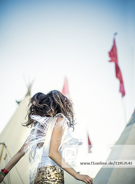 Seitenansicht einer jungen Frau bei einem Sommer-Musikfestival  die in goldenen  mit Pailletten bestickten Hotpants tanzt.
