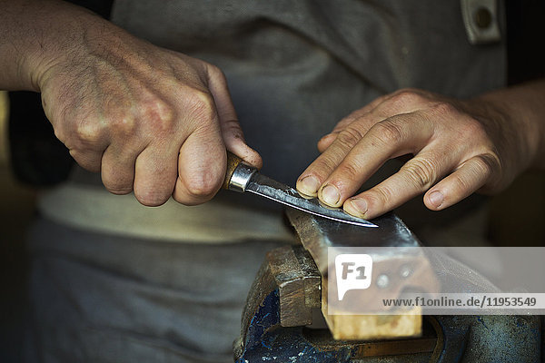 Nahaufnahme eines Holzschnitzers  der die Klinge eines Schnitzermessers an einem Lederriemen schleift  die Klinge nach unten drückt und seine Werkzeuge schleift.