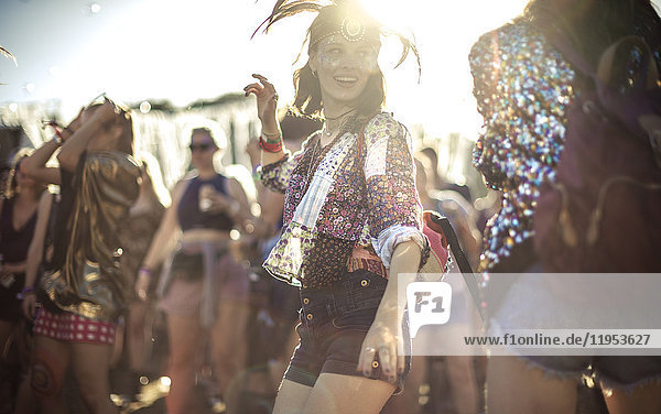 Junge Frau bei einem Sommer-Musikfestival mit Federkopfschmuck  die in der Menge tanzt.