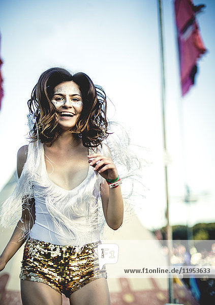Junge Frau bei einem Sommer-Musikfestival in goldenen  mit Pailletten bestickten Hotpants  geschminktes Gesicht  lächelt in die Kamera.