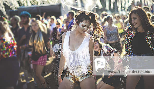 Junge Frau bei einem Sommer-Musikfestival  die in goldenen  mit Pailletten bestickten Hotpants unter der Menge tanzt.